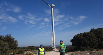 Two employees in front of the tower of a wind turbine